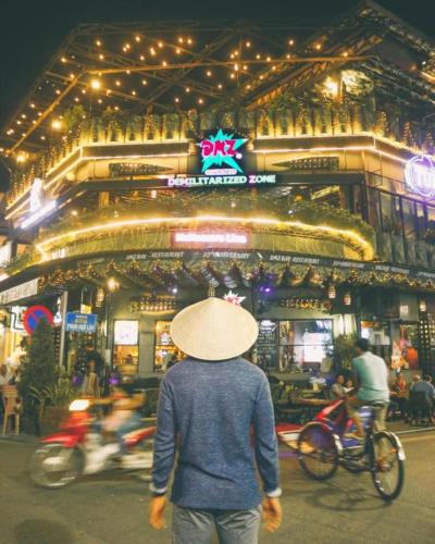 a man in a hat walking past a building with motorcycles at DMZ Hostel in Hue
