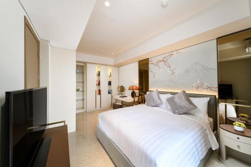 Oakwood Apartments PIK Jakarta في جاكرتا: غرفة نوم بسرير ابيض وتلفزيون بشاشة مسطحة