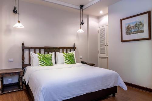 Schlafzimmer mit einem Bett mit weißer Bettwäsche und grünen Kissen in der Unterkunft At 21 Saladaeng in Bangkok