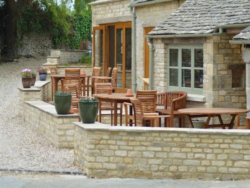 a patio with wooden tables and chairs and a building at The Plough Inn in Cheltenham