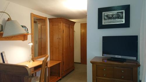 a living room with a tv and a desk with a dresser at Pension Landhaus Fischer in Maßweiler