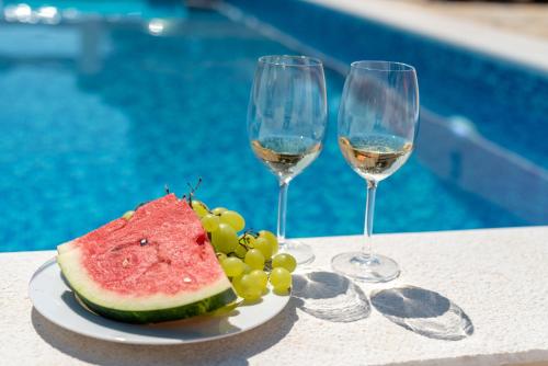twee glazen wijn en een bord watermeloen en druiven bij Eden Mediterranean House in Vrsine