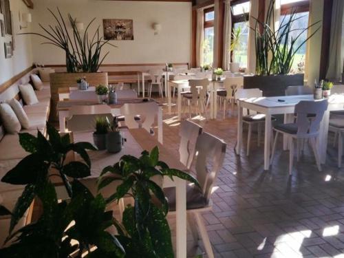 um restaurante com mesas brancas, cadeiras e plantas em Gasthof Ruckriegel em Seybothenreuth