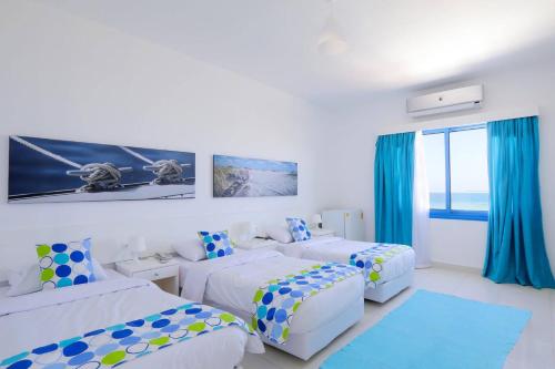 a white room with two beds and blue curtains at Lagoonie Lodge & Beach in Hurghada