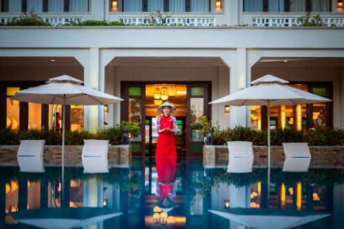 a woman in a red dress standing in front of a building at RiverTown Hoi An Resort & Spa in Hoi An