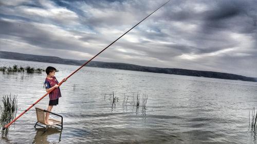 a young boy is standing in the water holding a pole at 19th Century Magical House in Galilee in ‘Eilabūn
