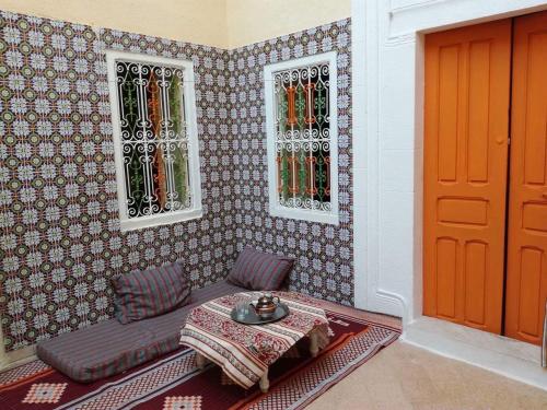 Zimmer mit einem Tisch, 2 Fenstern und einer Tür in der Unterkunft Dar EL Hamra Maison Typique in Mahdia