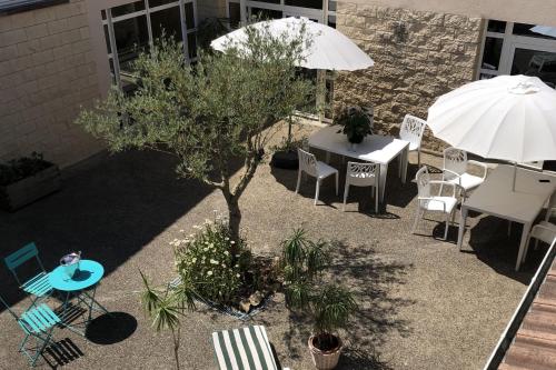 une terrasse avec une table, des chaises et un parasol dans l'établissement Patio Parc Résidence, à Argenton lʼÉglise