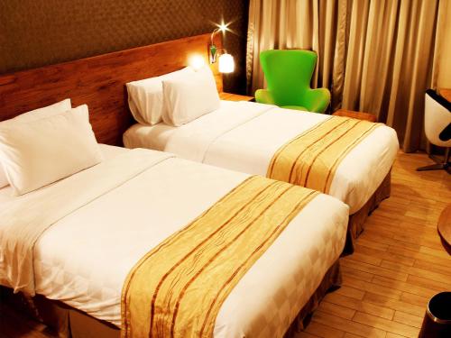 a hotel room with two beds and a green chair at Hariston Hotel&Suites, Pluit - Jakarta in Jakarta