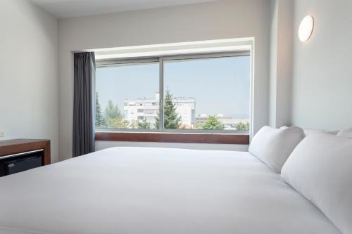 a bedroom with a white bed and a large window at B&B HOTEL e Apartamentos Felgueiras in Felgueiras