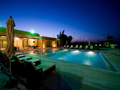ein Pool in der Nacht mit Stühlen und einem Sonnenschirm in der Unterkunft Amman Airport Hotel in Al Qasţal