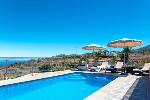 a swimming pool with chairs and umbrellas and the ocean at Casa la Viña in Puntagorda