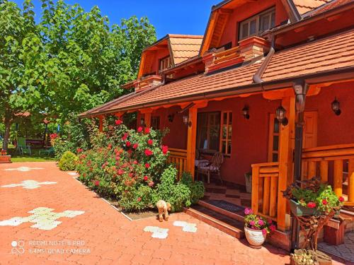 a dog standing outside of a house with flowers at Eko Apartmani in Bački Petrovac