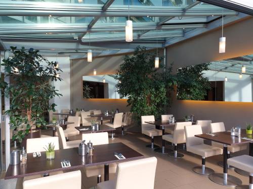 un restaurante con mesas, sillas blancas y plantas en City Hotel Stuttgart en Stuttgart