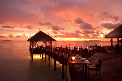 a pier with tables and chairs on the water with a sunset at Sun Siyam Iru Fushi with Free Transfer in Manadhoo