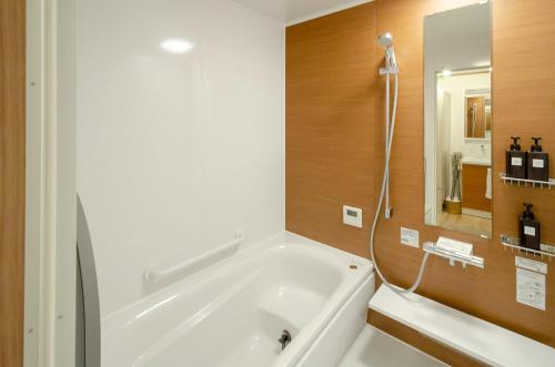 baño con bañera blanca grande y espejo en 箱館宿 観月-Mizuki-伝統的建築物の宿-最大8名宿泊可能, en Hakodate