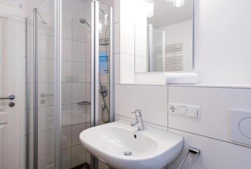 La salle de bains blanche est pourvue d'un lavabo et d'une douche. dans l'établissement Appartement Lille Kamp 1, à Westerland
