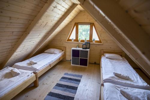 two beds in a wooden attic room with a window at Dadaj Summer Camp - całoroczne domki Rukławki in Biskupiec