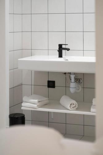 a white bathroom with a sink and towels on shelves at Monsieur Miot Concept Hotel - Bastia centre in Bastia
