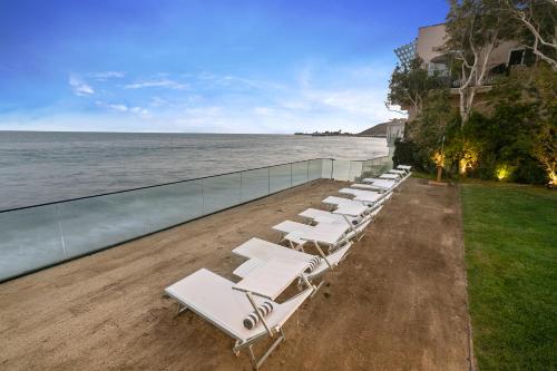 a row of white lounge chairs on the beach at SA Carbon Beach Suites in Malibu