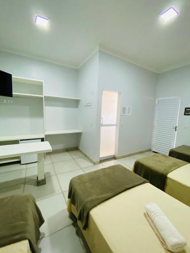 a room with two beds and a desk and a television at Hotel Pousada Marra in Catalão