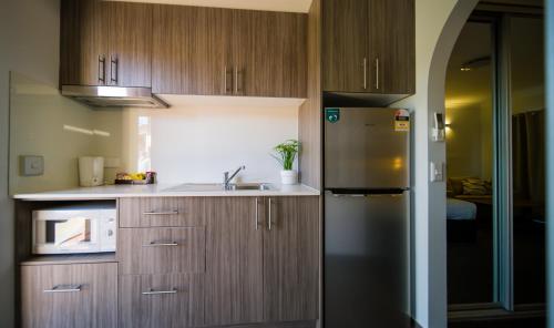 a kitchen with wooden cabinets and a stainless steel refrigerator at Hamilton's Queanbeyan Motel in Queanbeyan