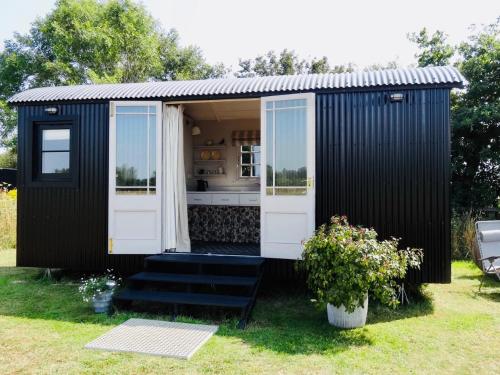 a black shed with white doors and a window at The Oaks Glamping - Rubie's Shepherds Hut in Colkirk