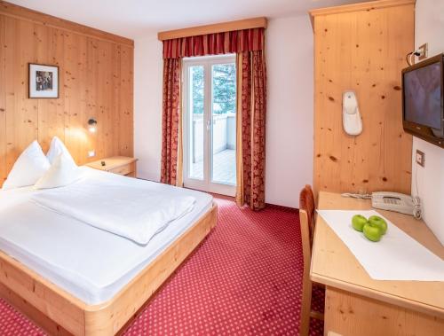 a bedroom with a bed and a desk and a television at Hotel Eichenhof in Tirolo
