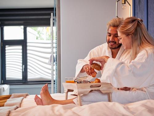 a man and a woman sitting in bed eating food at De Maasparel Nextdoor Maassuites in Arcen