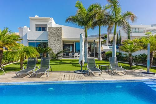a pool with chairs and umbrellas next to a house at Villa Eleonora, Luxury Villa with Heated Pool Ocean View in Adeje, Tenerife in Adeje