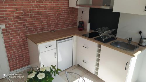 a small kitchen with white cabinets and a brick wall at Appartement tout confort au calme avec jacuzzi in Mouguerre