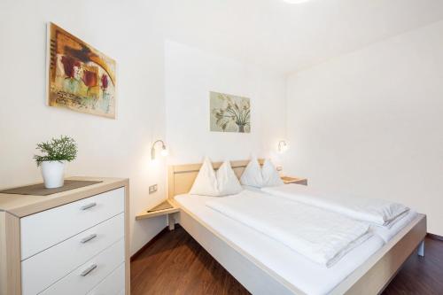 a white bedroom with a bed and a dresser at Tischlerhof - Typ C in Tirolo