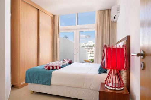 a bedroom with a bed with a red lamp and a window at Muthu Clube Praia da Oura in Albufeira
