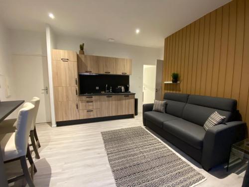 a living room with a black couch and a kitchen at Gîtes de la Porte Saint Martin in Châteauroux