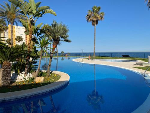 a large blue swimming pool with palm trees and the ocean at Mi Capricho, Luxury Apartment in Mijas Costa