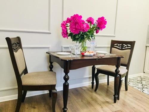 a table with two chairs and a vase of pink flowers at Апартаменти Кобилянська 9 in Chernivtsi