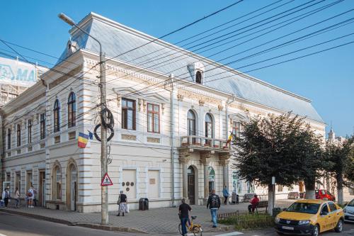 a large white building on a street with a yellow taxi at Buchenland Hotel in Câmpulung Moldovenesc