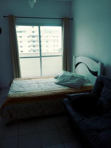 a bed in a room with a window and a couch at Mordomia no Guarujá in Guarujá