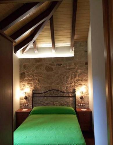 a bedroom with a green bed with a stone wall at Casa Casoa in Piornedo