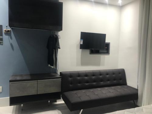 a living room with a black leather couch and a tv at Ipanema Prudente Studio in Rio de Janeiro