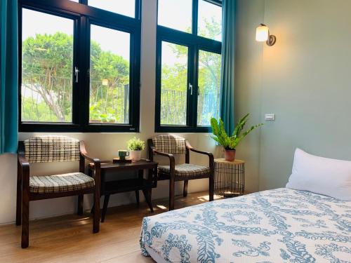 a bedroom with a bed and chairs and windows at OYAJI Guesthouse 歐野基民家宿泊 in Tainan