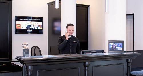 Un hombre sentado en un escritorio hablando por un teléfono celular en Victor's Residenz-Hotel Gummersbach, en Gummersbach