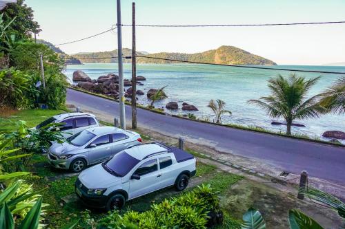 deux voitures garées sur une route à côté d'une plage dans l'établissement Pousada Piquara, à Mangaratiba