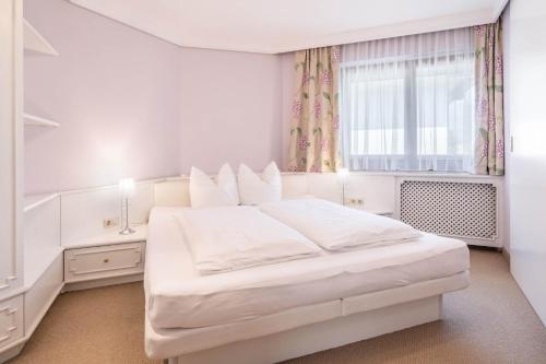 a white bedroom with a large white bed and a window at Appartements Mair in Mayrhofen