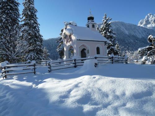 a small white chapel with a fence in the snow at Pension Karner in Mittenwald