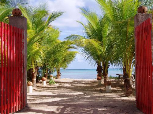 a red fence on a beach with palm trees at Pousada Vida Sol in São Miguel dos Milagres