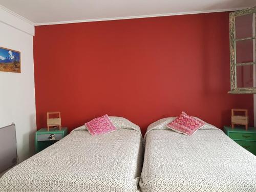two beds in a room with a red wall at Eco-Hostal Tambo Verde in Santiago