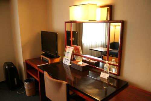 a room with a desk with a television and a mirror at Konaya Hotel in Kofu