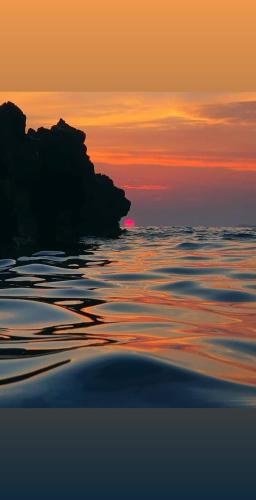 a sunset over the ocean with a rock in the water at Apartments Dragišić in Sveti Stefan