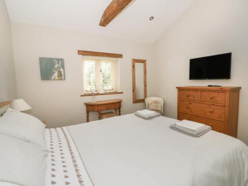 a bedroom with a white bed with a dresser and a tv at Golson Stable in Spalding